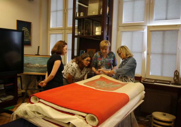 Przy galowej banderze; od lewej stoją: Anna Pawlak z Zespołu ds. Projektów - Dział Nauki UMG, Arleta Gałązka – kustosz „Daru Pomorza” (Narodowe Muzeum Morskie w Gdańsku), Joanna Stasiak – kustosz Sali Tradycji UMG i konserwator tkanin Mariola Ratajczyk