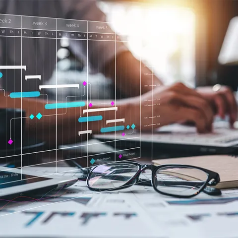 dłonie na klawiaturze laptopa, okulary na blacie biurka 